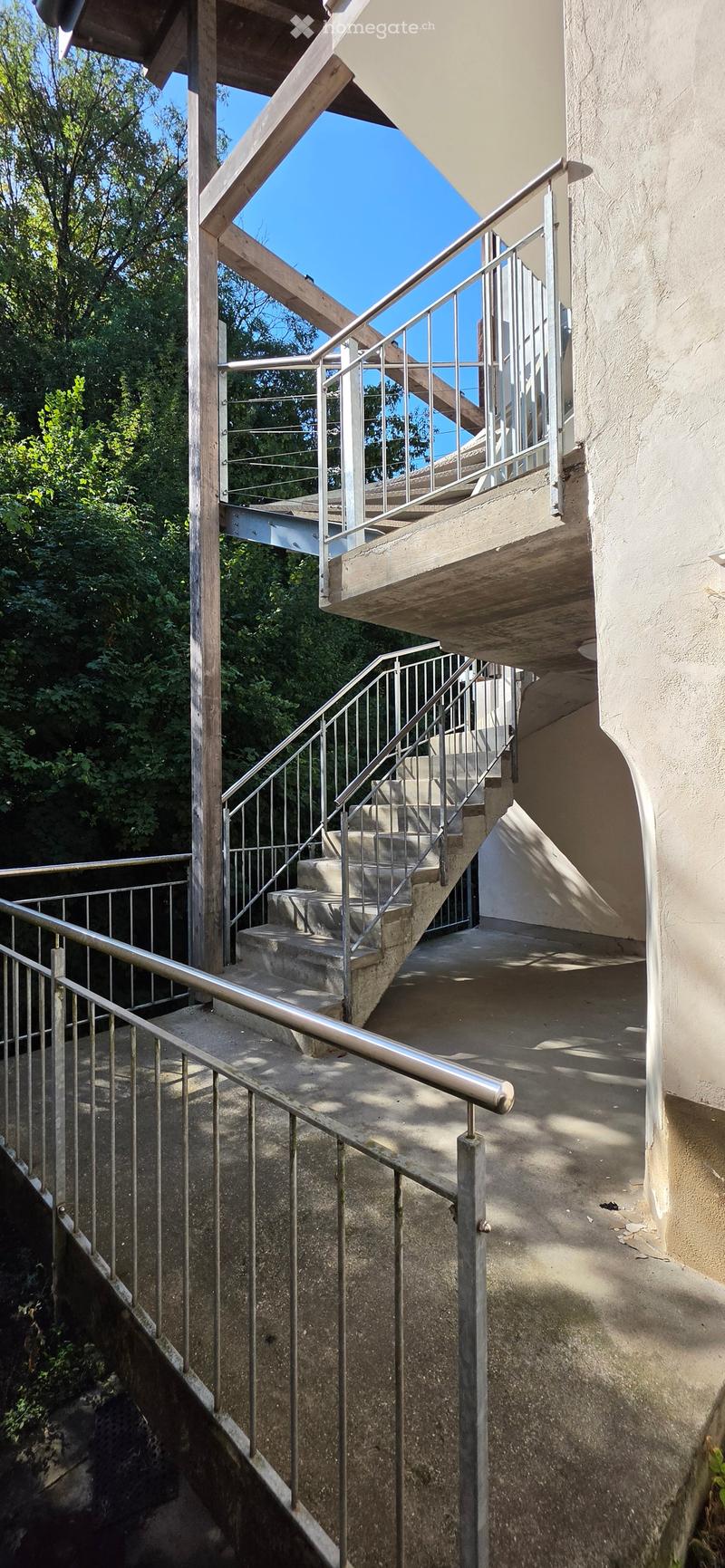 An outdoor staircase with metal railings and concrete steps, leading up to a raised ground floor area.