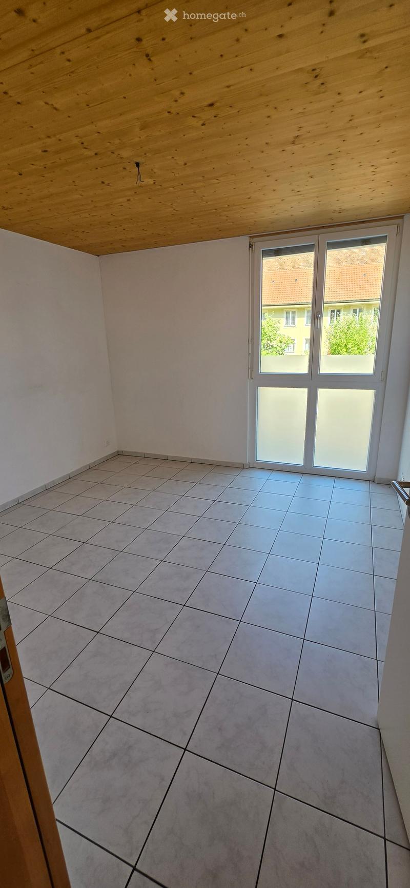 Empty room with tiled floor, white walls, and a large sliding glass door leading outside.