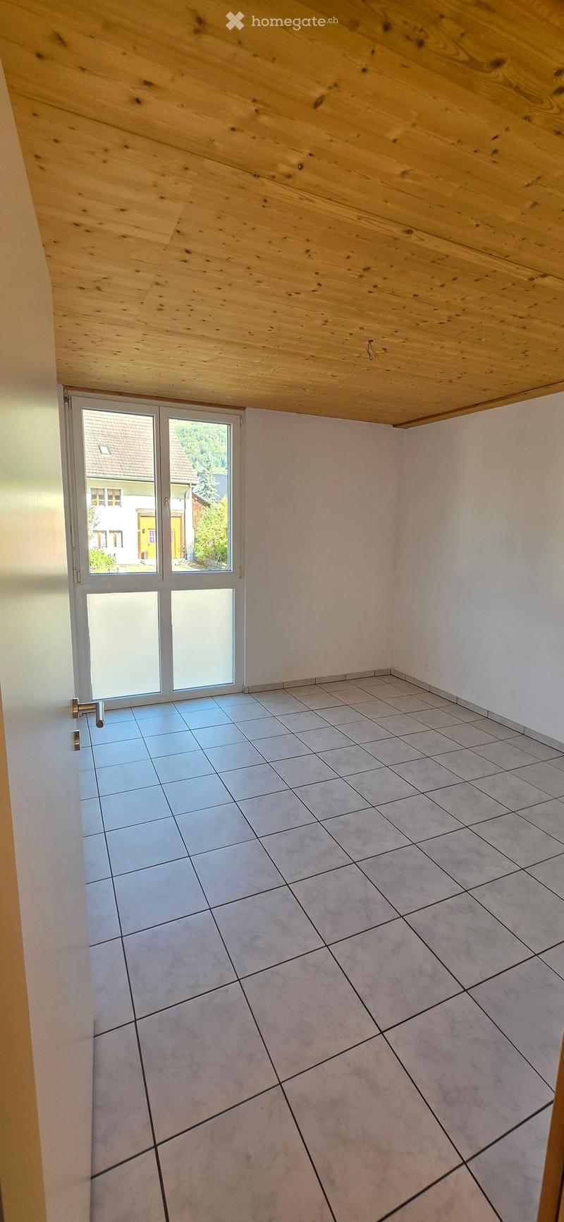 Empty room with light grey tiled floor, white walls, and a large sliding glass door leading outside.