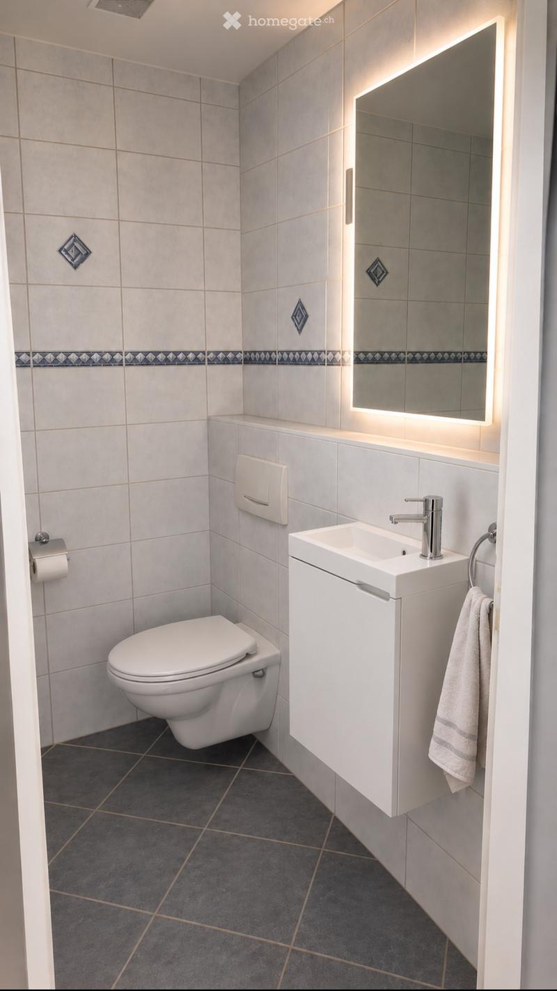 Modern bathroom with white tiles, a toilet, a sink with a modern faucet, a large illuminated mirror, and a towel hanging on a ring.