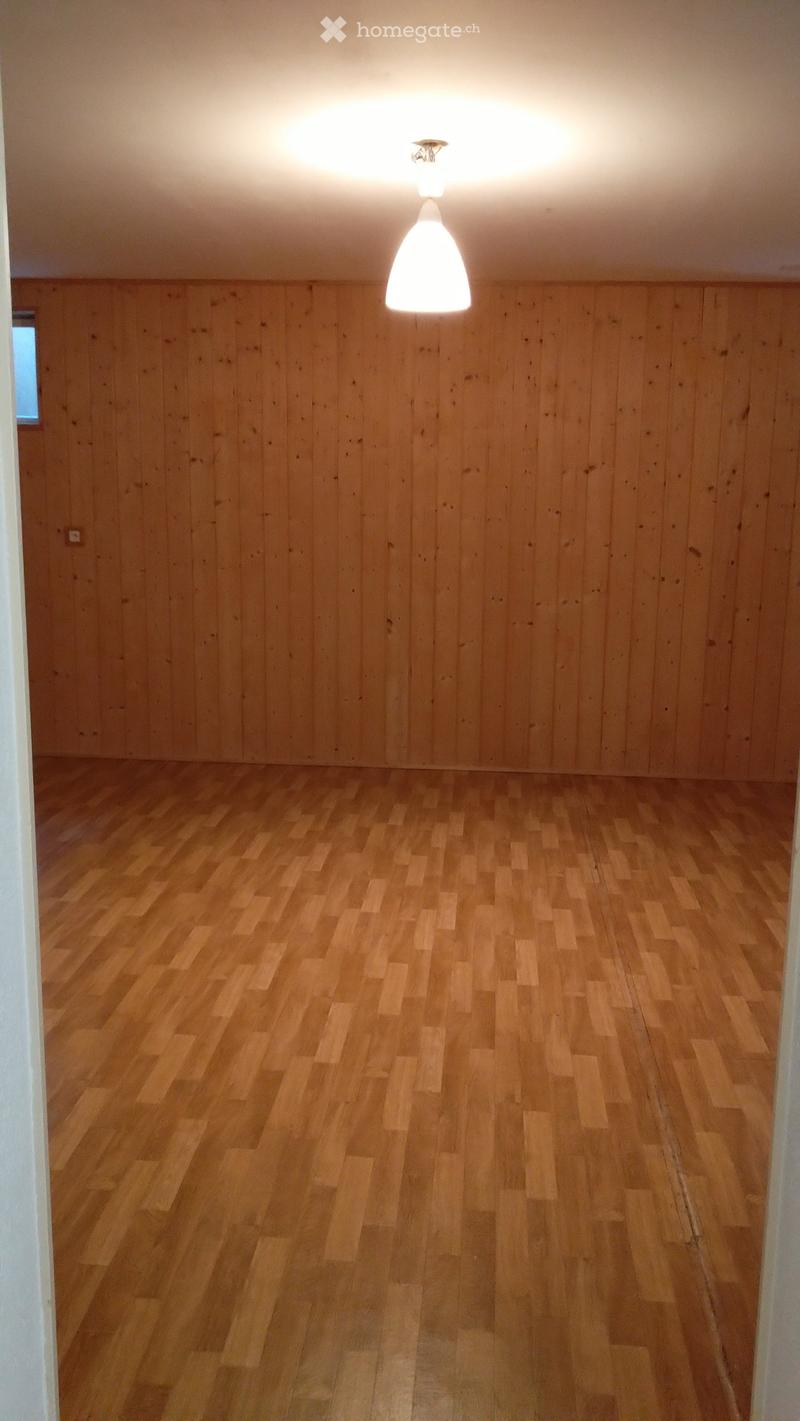 Empty room with wooden walls and floor, single pendant light fixture, and a small window on one wall.