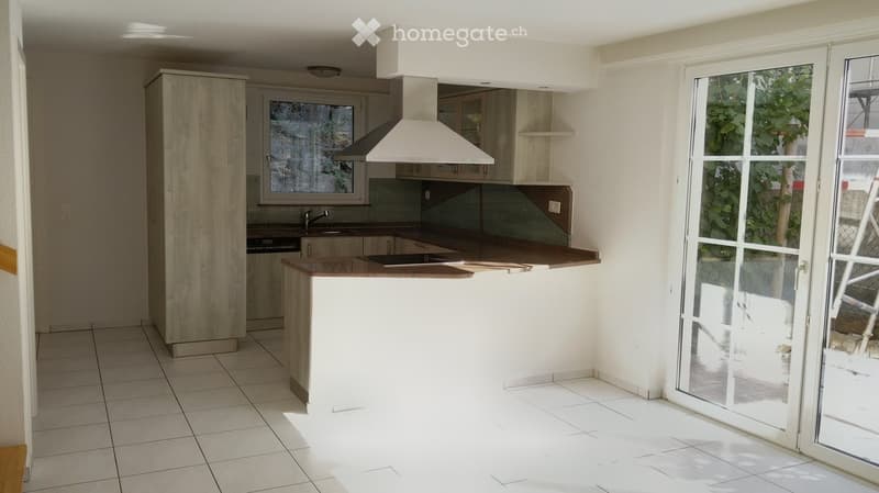 Modern kitchen with white cabinets, a central island, and a large window. Features include a range hood, sink, and tiled flooring.