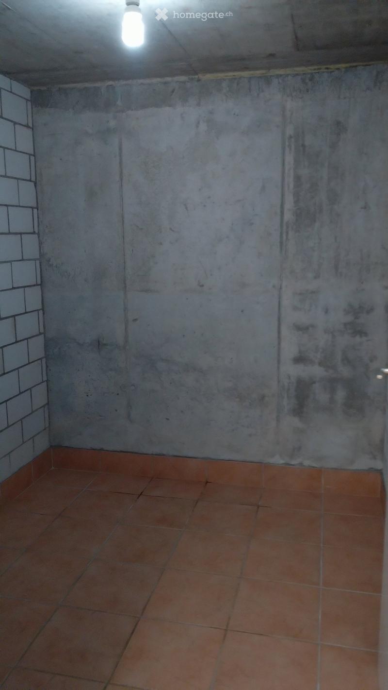 Empty room with concrete walls and tiled floor, illuminated by a single ceiling light.