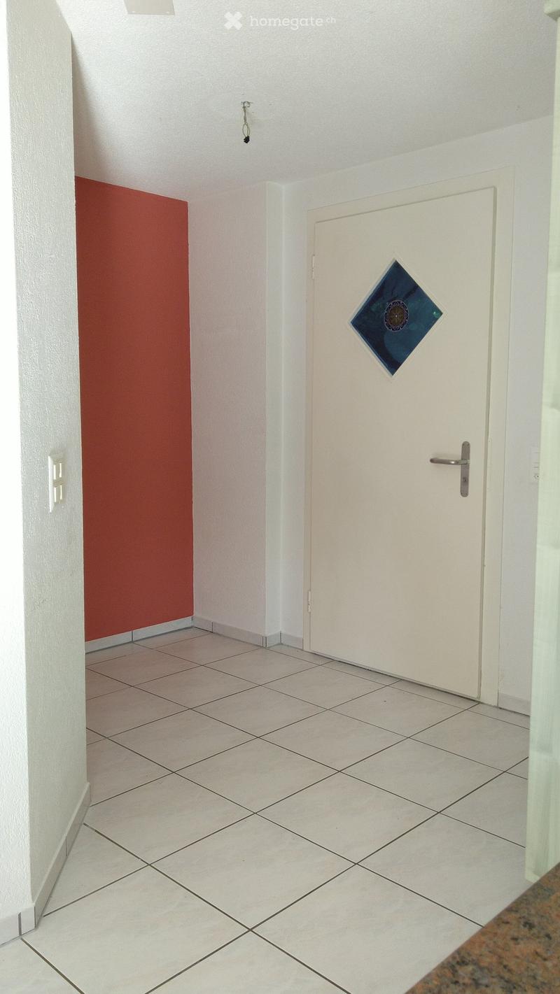 A clean, tiled hallway with white walls, a red accent wall, and a white door featuring a decorative glass panel.