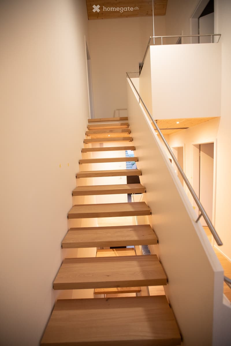 Modern wooden staircase with a sleek metal railing, white walls, and warm lighting.
