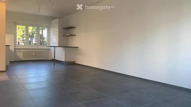 Empty kitchen with white cabinets, dark tiled floor, large windows, and a radiator under the windows.