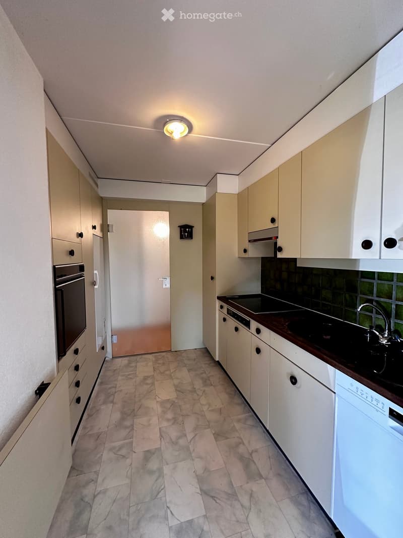 Modern kitchen with light-colored cabinets, a dark countertop, and a tiled floor. Features include a sink with a faucet, an oven, and a dishwasher.