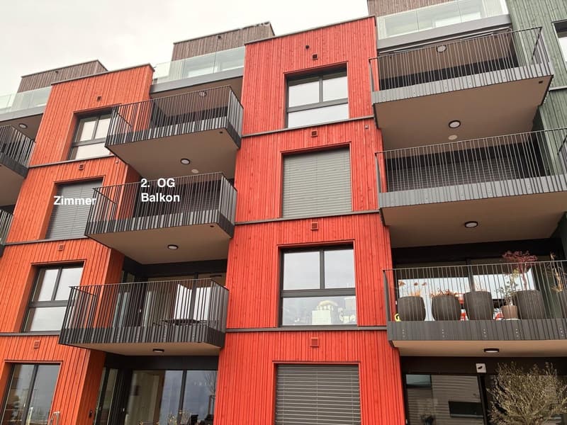 Modern multi-story building with red wooden facade, multiple balconies, large windows, and modern railings.