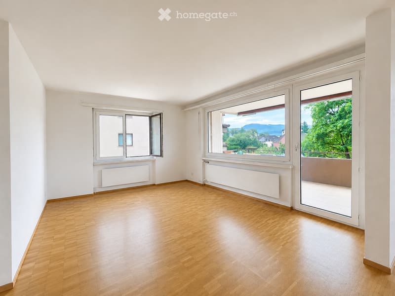 Empty room with wooden flooring, white walls, large windows, and a balcony door leading to a terrace.