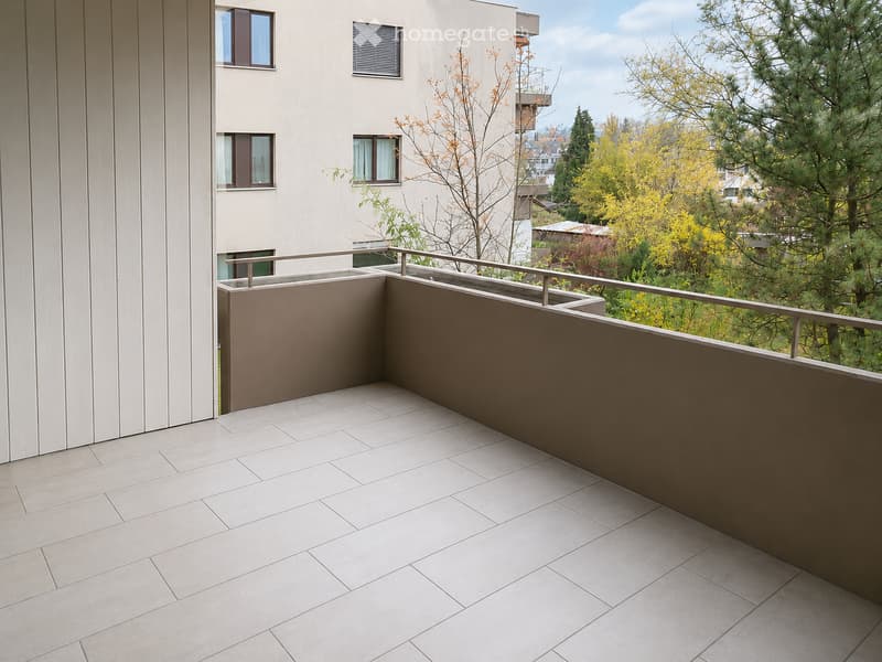 Modern balcony with tiled floor, low railing, and a view of trees and buildings.