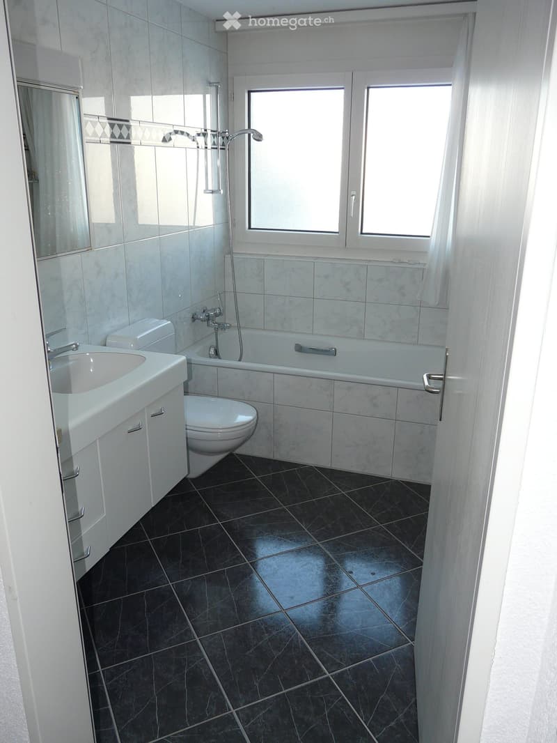 Modern bathroom with white tiles, black tiled floor, sink, toilet, bathtub, and large window with white frame.