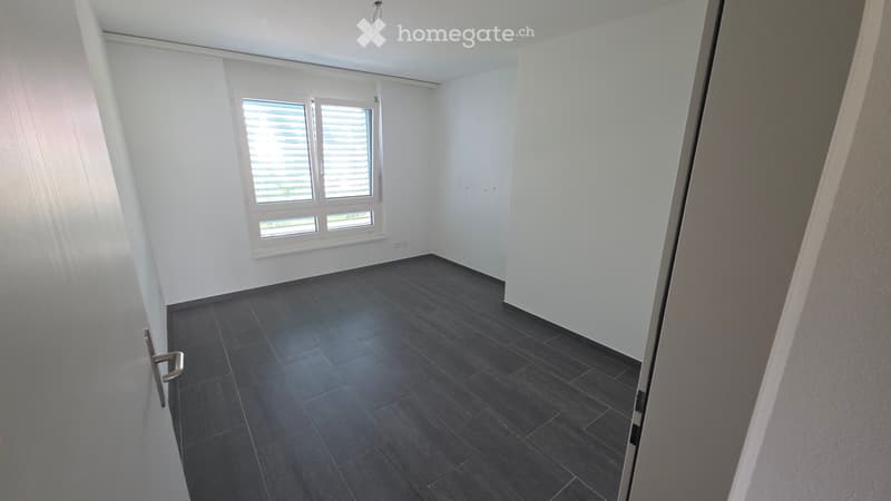 Empty room with dark tiled flooring, white walls, and a window with blinds. No furniture or equipment is present.