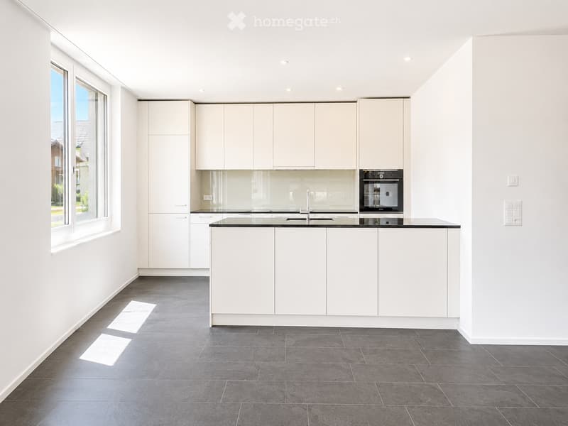Modern kitchen with white cabinets, black countertop, and stainless steel appliances, featuring large windows and a central island.