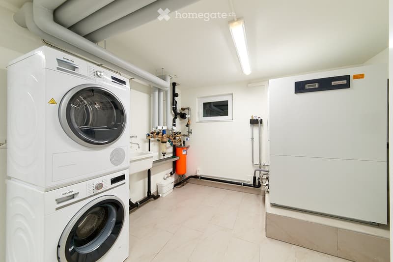 Laundry room with two Siemens washing machines and a dishwasher. It has white tiled flooring, white walls, and modern appliances.