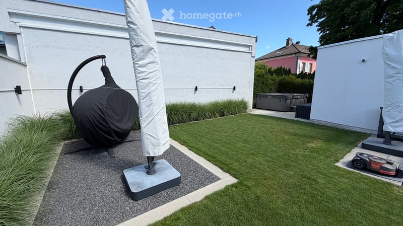 Well-maintained garden with a lawn, patio area, covered outdoor furniture, and a robotic lawnmower.