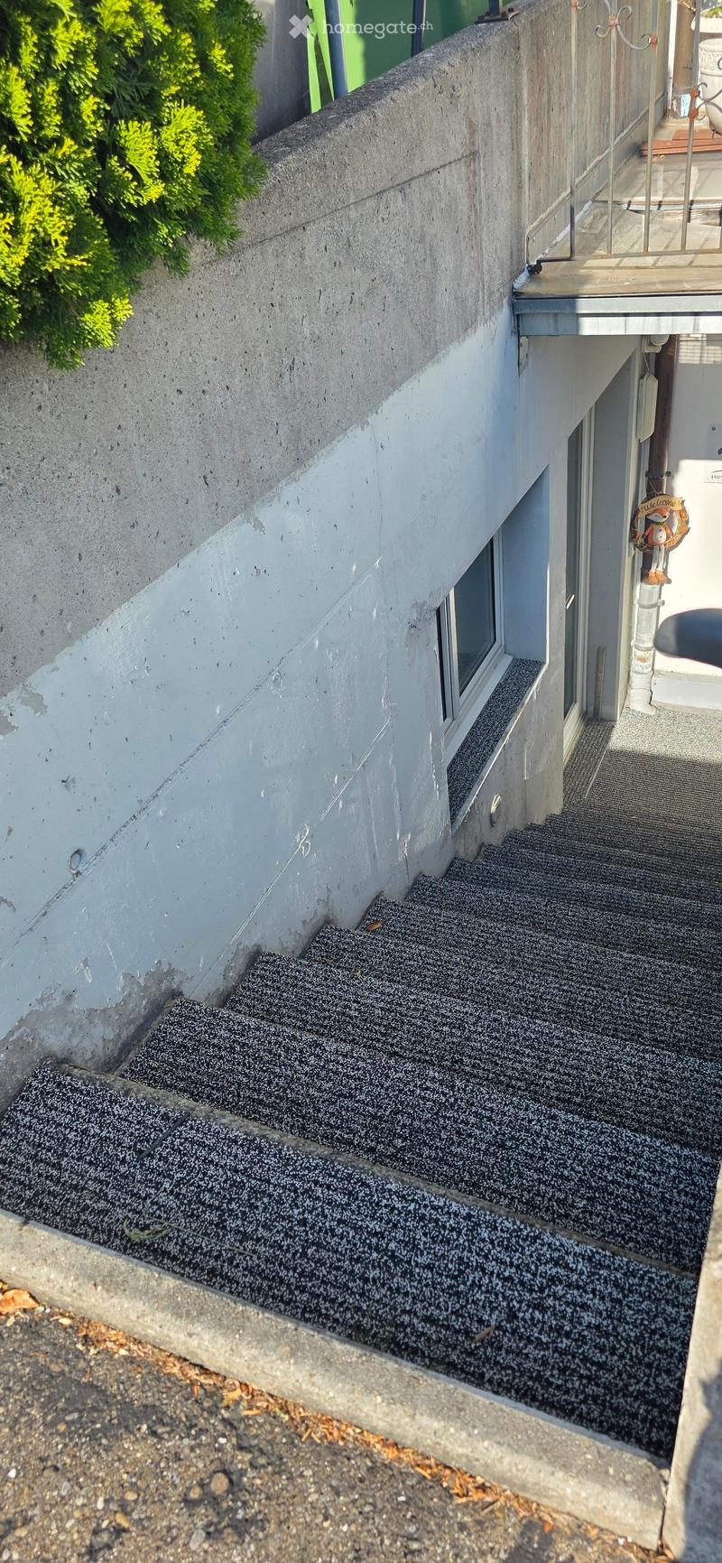 Staircase leading up to a balcony area with a railing and greenery visible on the left side.