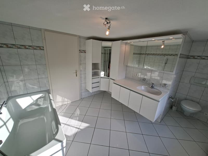 Modern bathroom with white tiles, a bathtub, a sink with a mirror cabinet, and a toilet. The space features built-in storage cabinets and a sleek design.