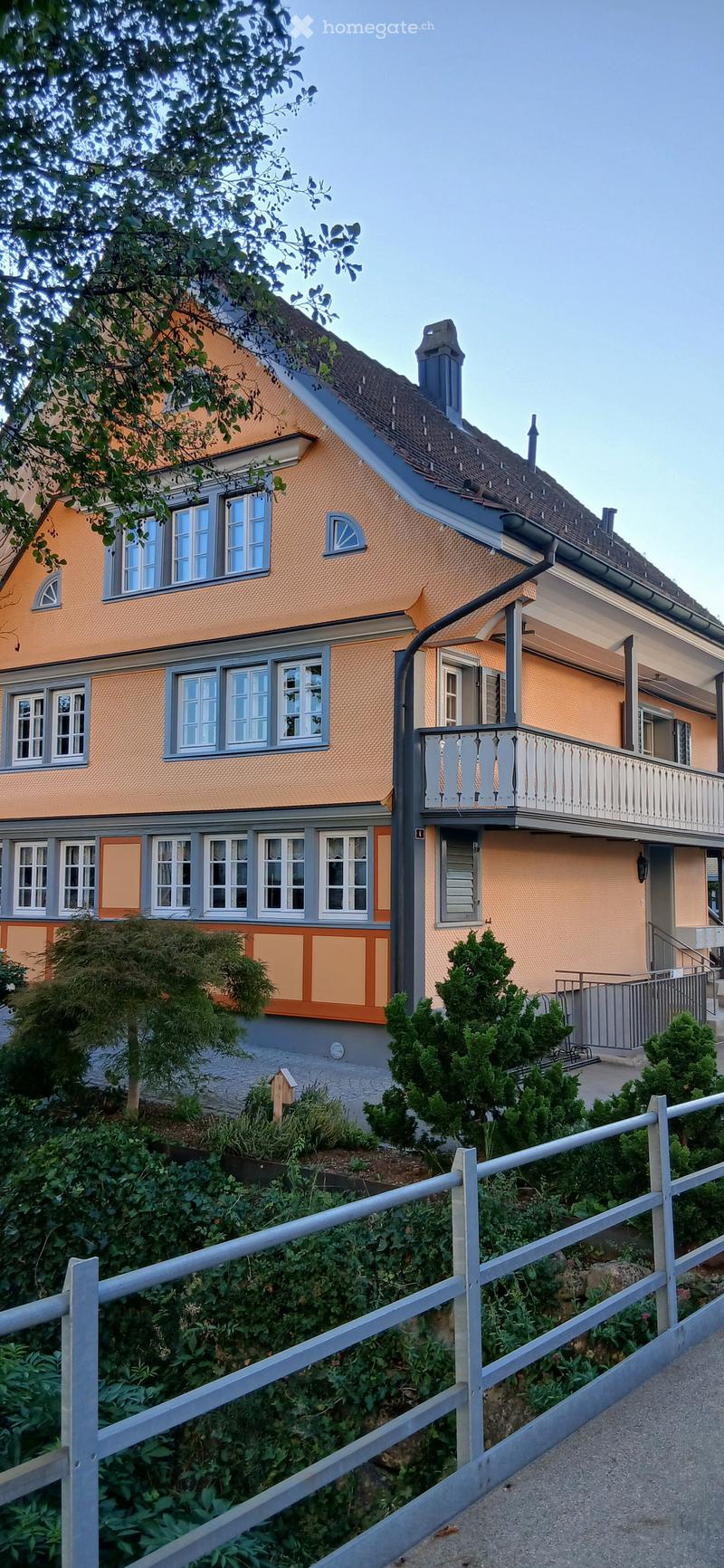 Two-story house with orange and grey exterior, multiple windows, and a balcony on the upper level.