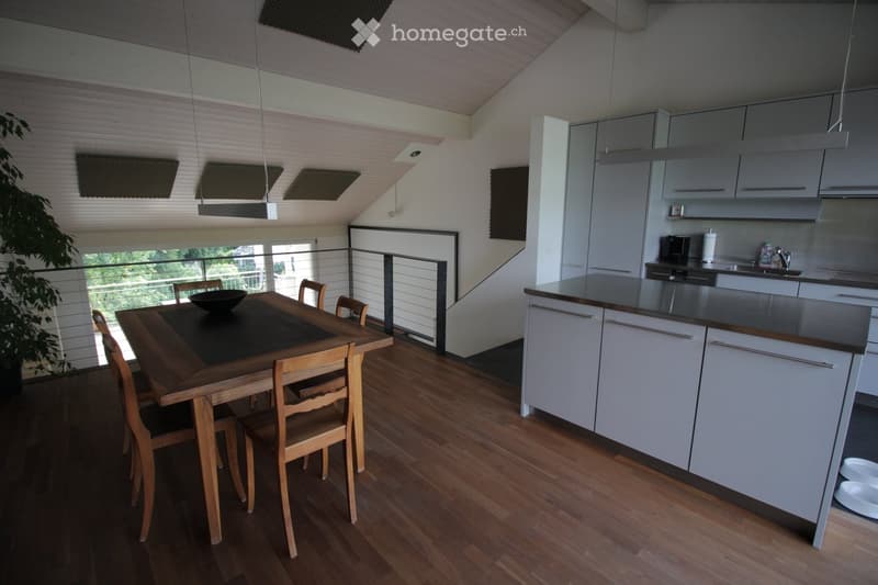 Open-plan kitchen and dining area with white cabinets, wooden dining table, chairs, and a view through a glass railing.