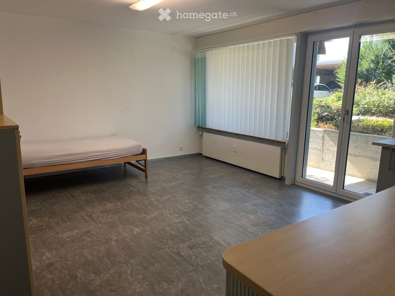 A small, furnished bedroom with a single bed, wooden flooring, and large sliding glass doors leading to a balcony.