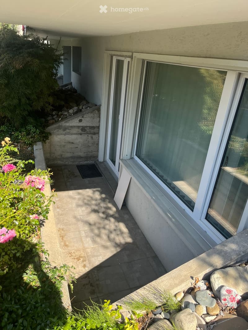 Balcony with tiled floor, large window, and small garden area with rocks and plants.