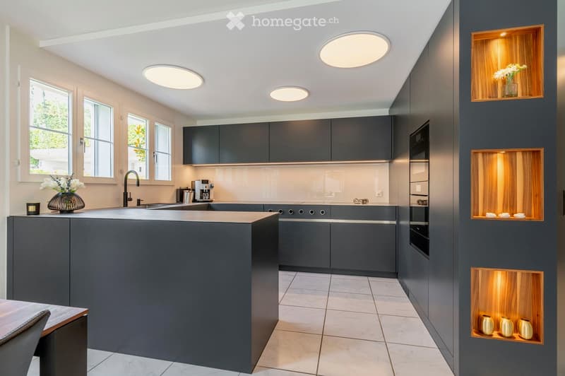 Modern kitchen with grey cabinets, a central island, and built-in appliances. Features include a sink with a modern faucet, a coffee maker on the counter, and decorative vases on the island and shelves.