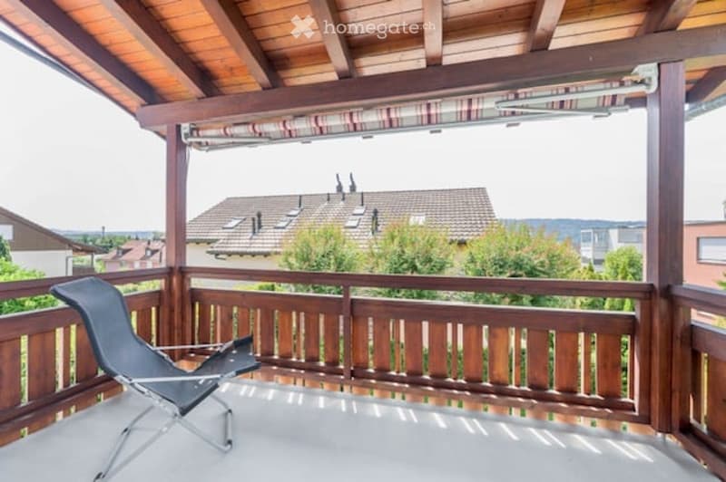 Wooden balcony with a lounge chair, overlooking a residential area with houses and trees.