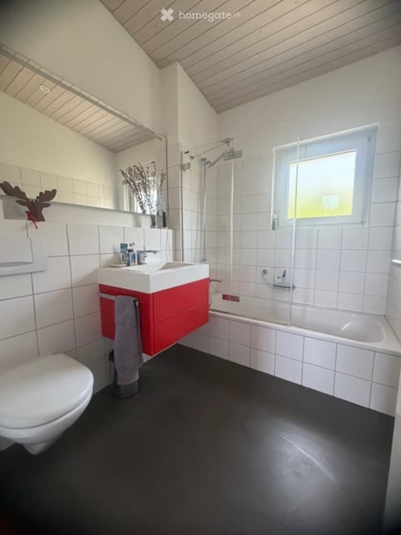 Modern bathroom with white tiles, black floor, red vanity cabinet, sink, bathtub, toilet, and a window providing natural light.