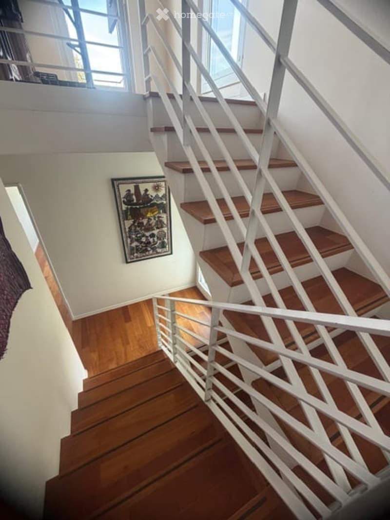 Wooden staircase with white metal railings, light-colored walls, and a framed picture on the wall.