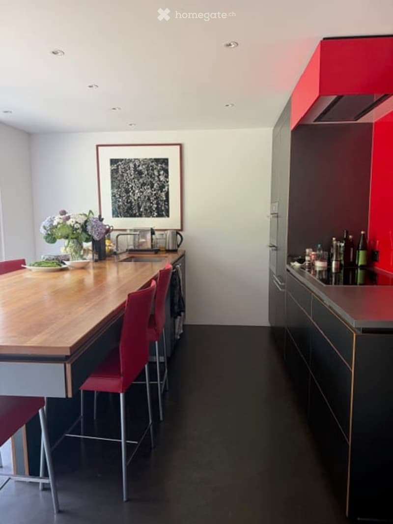 Modern kitchen with a wooden island, red bar stools, sleek black cabinets, and a stainless steel sink.