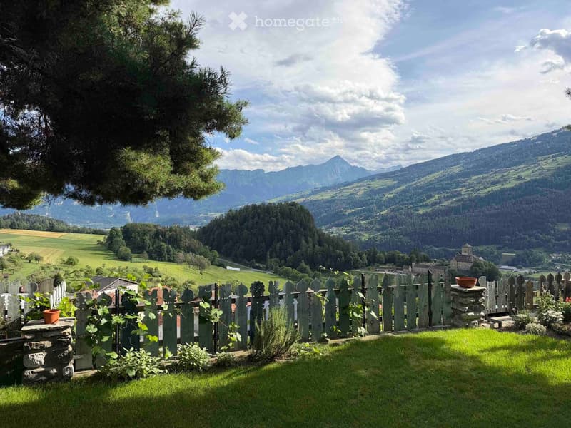 A serene garden with a wooden fence, lush green grass, and a scenic mountain view in the background.