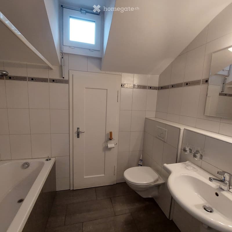 Bathroom with a bathtub, toilet, sink, mirror, and toilet paper holder. The room has tiled walls and a skylight window.