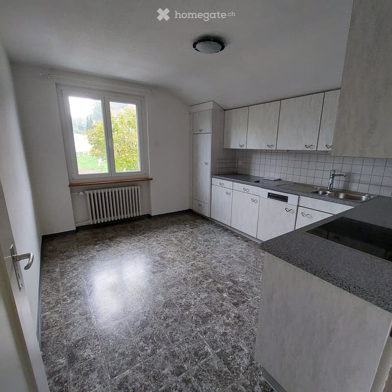 Empty kitchen with white cabinets, granite tiled floor, and a window overlooking a green area.