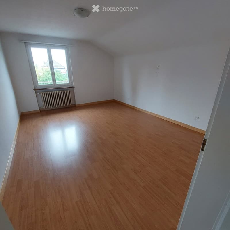 Empty room with wooden flooring, white walls, and a window with a radiator below it.