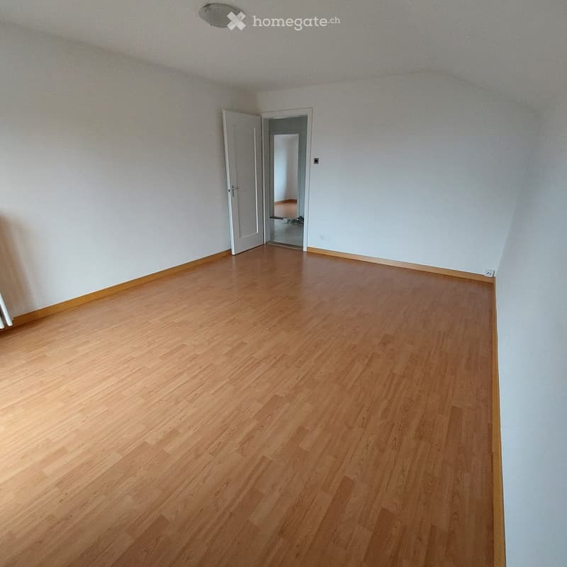 Empty room with light wooden flooring and white walls, featuring an open doorway leading to another room.