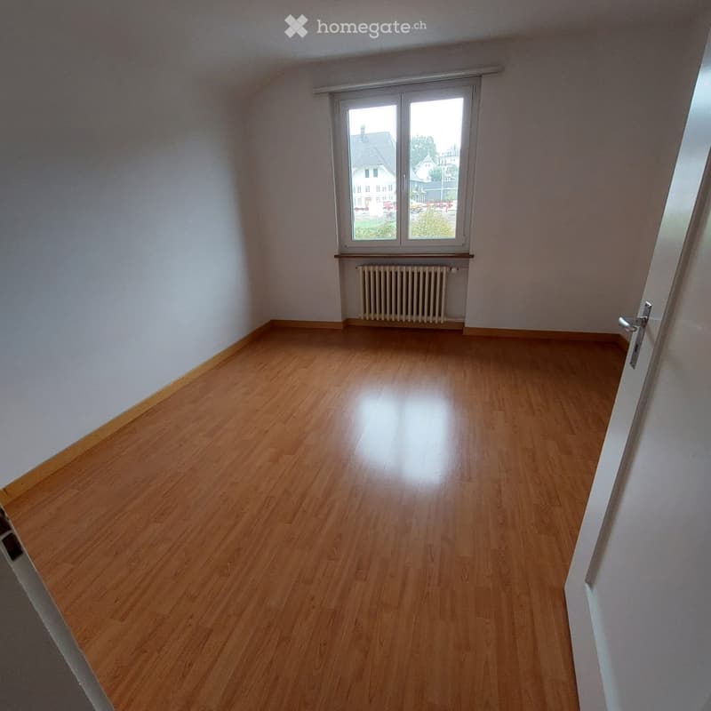 Empty room with wooden flooring, white walls, a window with blinds, and a radiator below the window.