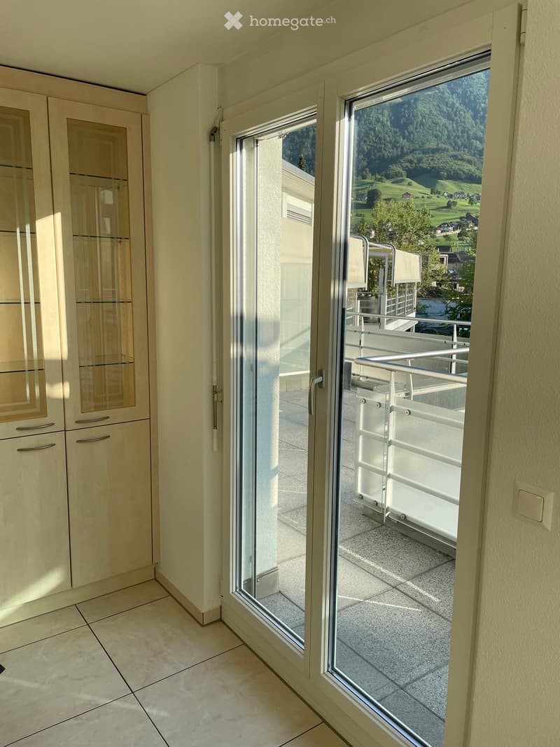 View of a balcony area with a glass door leading from an interior space, showing a scenic outdoor view of green hills and trees.