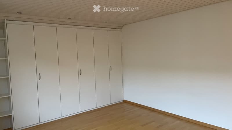 Empty room with light-colored wooden flooring and white walls, featuring built-in white closet units with multiple doors and shelves.