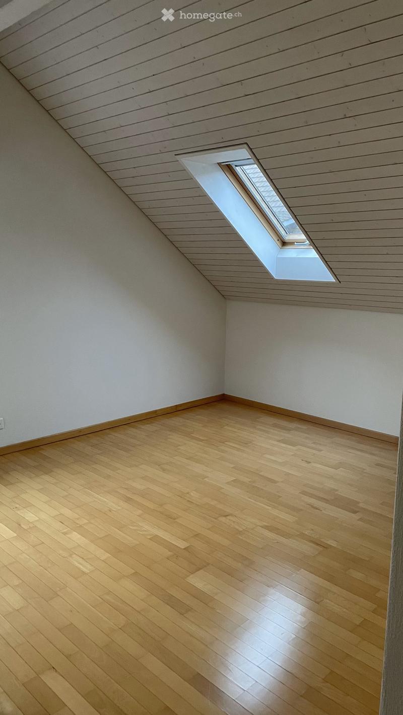 Empty room with wooden flooring and white walls, featuring a skylight window in the slanted ceiling.