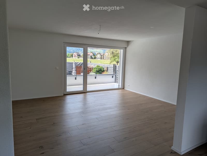Empty room with wooden flooring, white walls, and large sliding glass doors leading to a balcony with a scenic view.