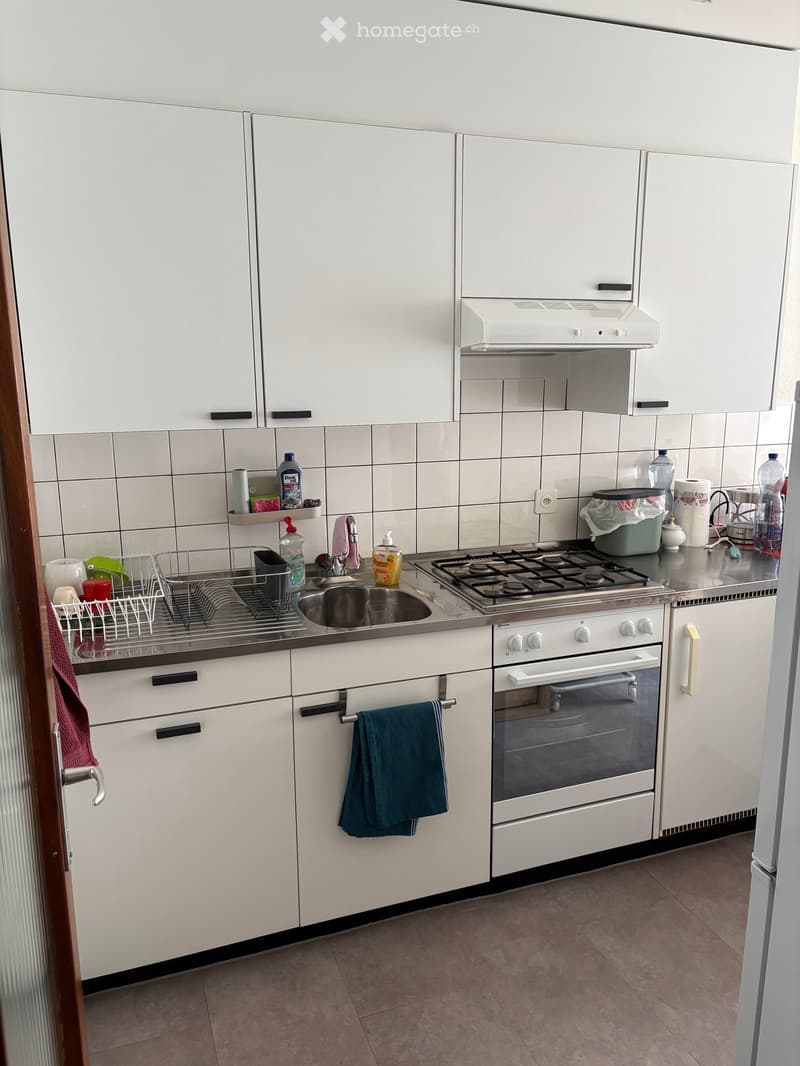Modern kitchen with white cabinets, stainless steel sink, gas stove, and various kitchen items on the counter.