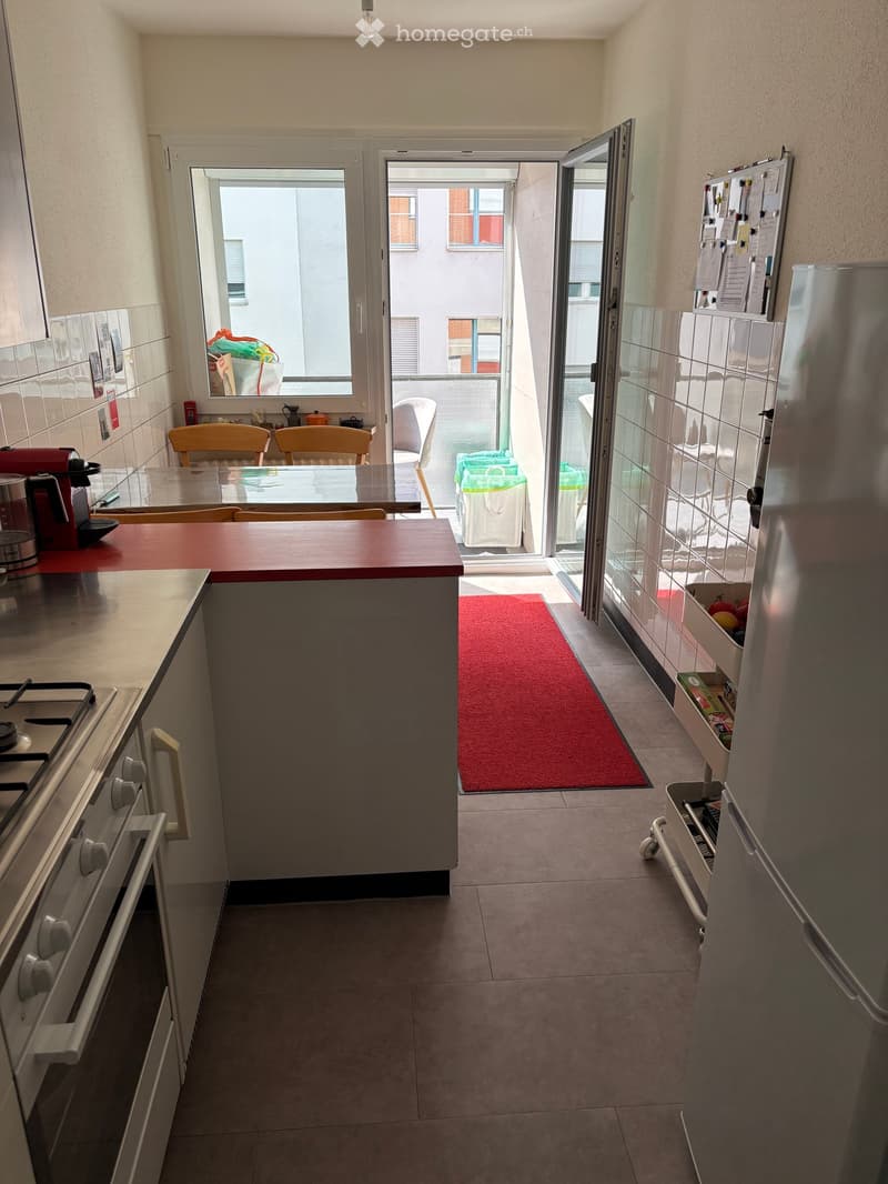 Modern kitchen with a central island, stove, refrigerator, and seating area leading to a balcony.