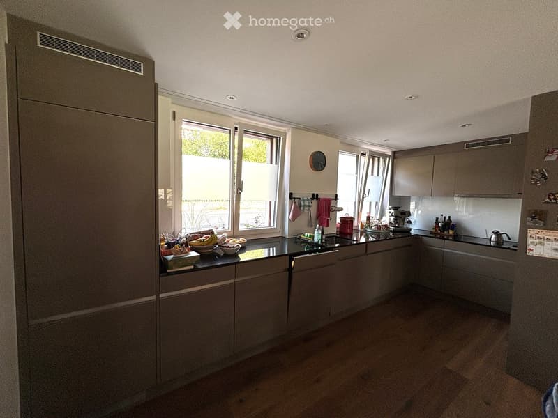 Modern kitchen with grey cabinets, black countertops, and stainless steel appliances. Features include a refrigerator, sink, coffee maker, and various kitchen items on the counter.
