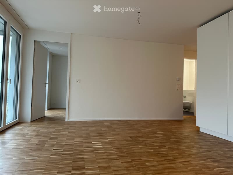 Empty room with wooden flooring, white walls, and large windows. No furniture or equipment is present.