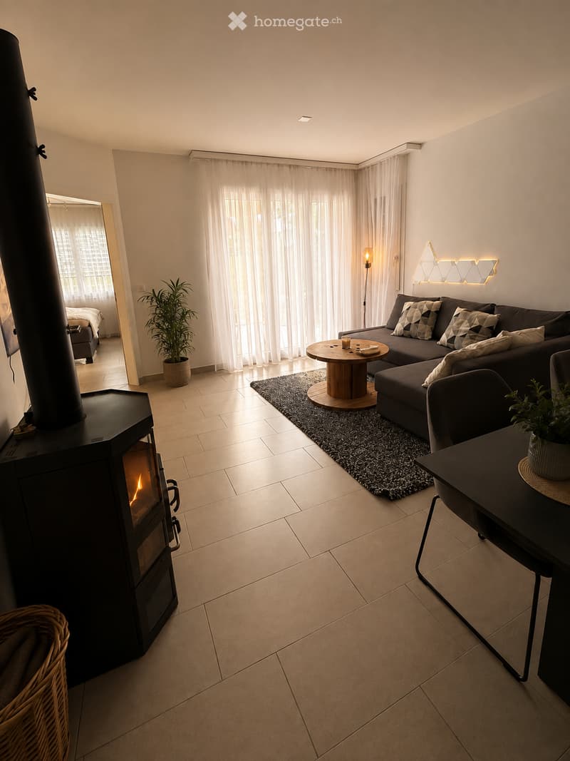Modern living room with a dark grey sectional sofa, wooden coffee table, floor lamp, fireplace, and large windows with sheer curtains.
