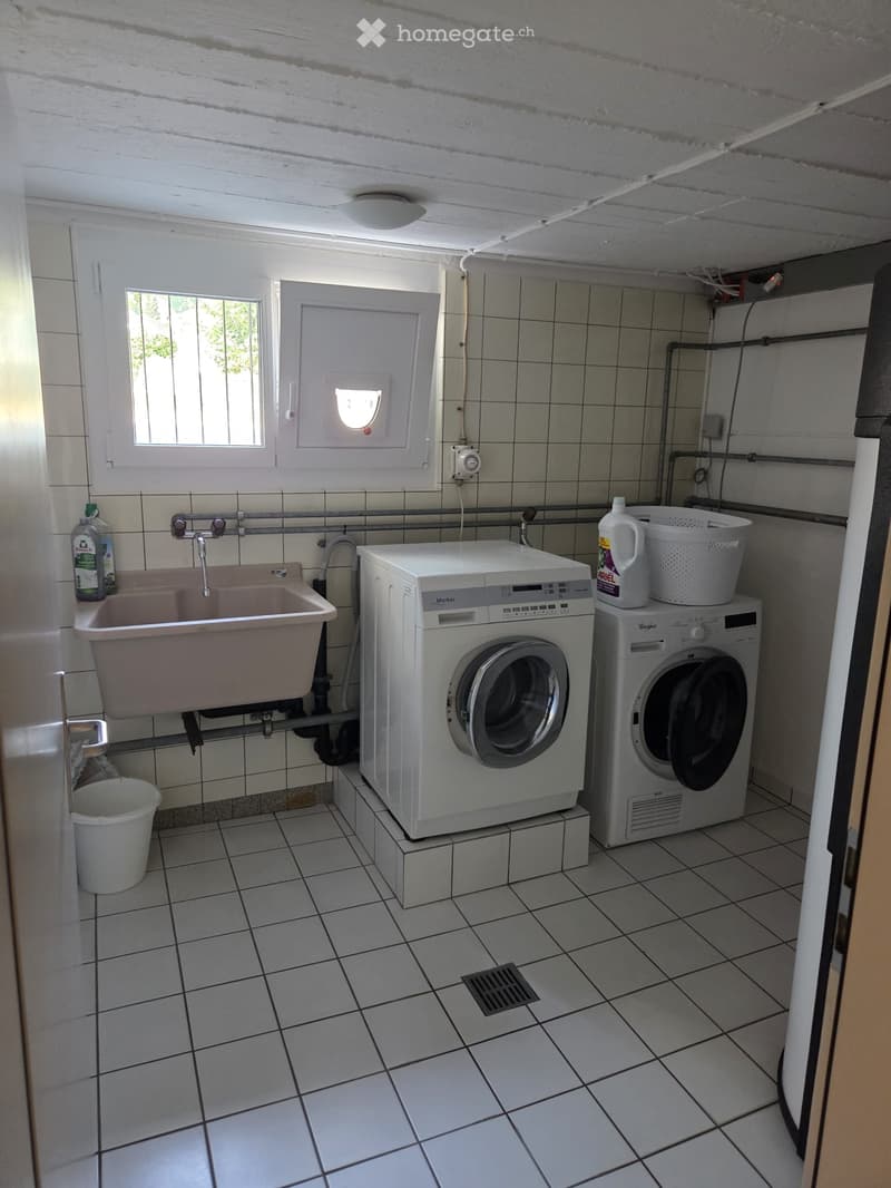 Utility room with tiled walls and floor, featuring a washing machine, sink, and laundry basket.