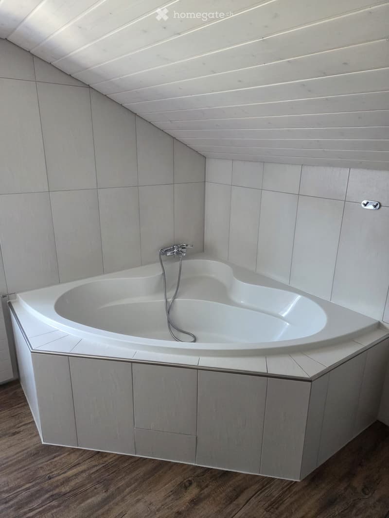 Modern bathroom with a corner bathtub, sleek grey tiles, and a wooden floor.