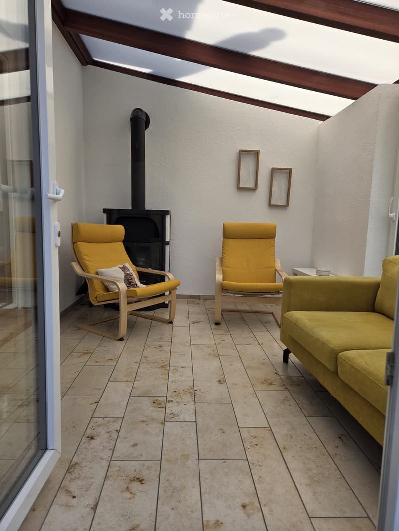Balcony with tiled floor, wooden slatted ceiling, fireplace, two yellow chairs, and a yellow sofa.