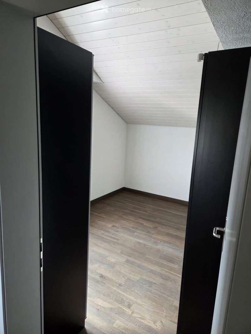 Empty room with wooden flooring, white walls, and a slanted white ceiling. No furniture or equipment visible.