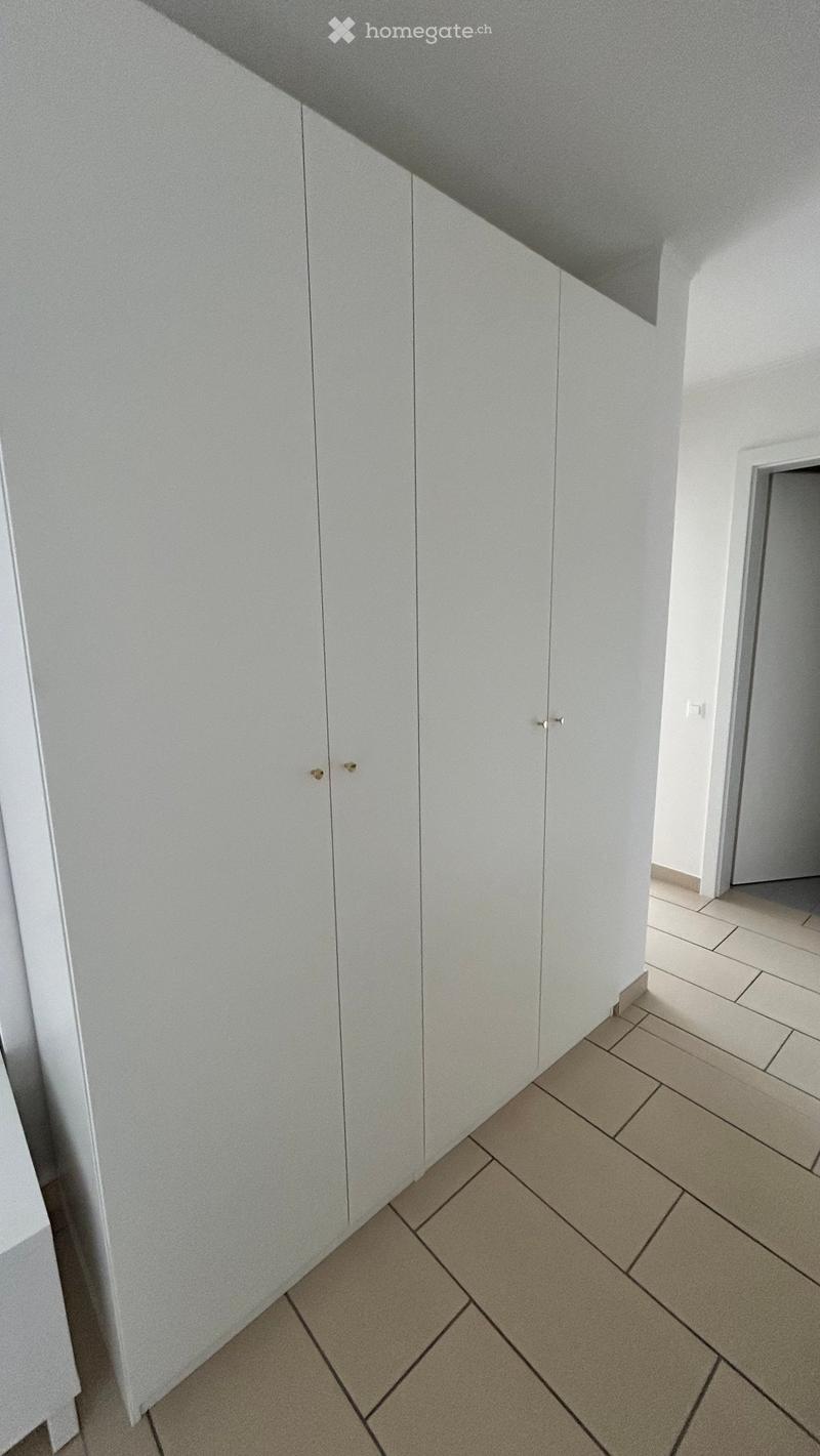 A clean, modern hallway with white walls, beige tiled flooring, and built-in white storage cabinets with gold handles.